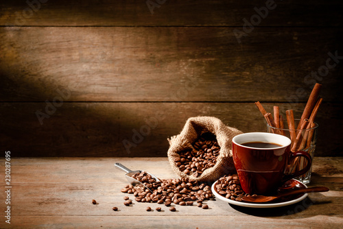 A Cup of black coffee with coffee bean bag and cinnamon on wooden floor with copyspace in background