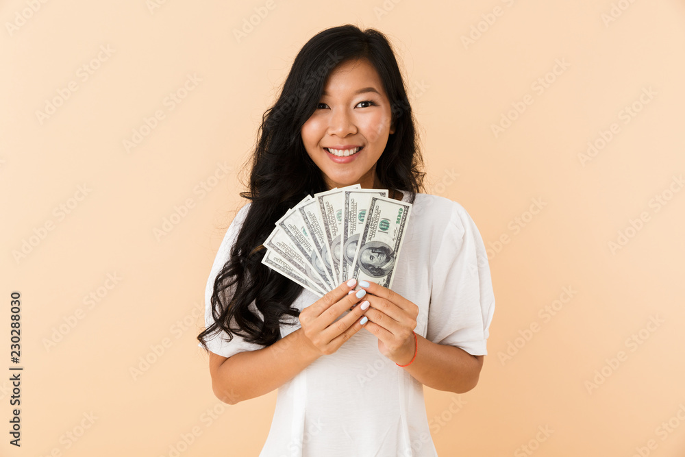 Happy asian woman posing isolated over beige wall background holding money. Happy asian woman posing isolated over beige wall background holding money.