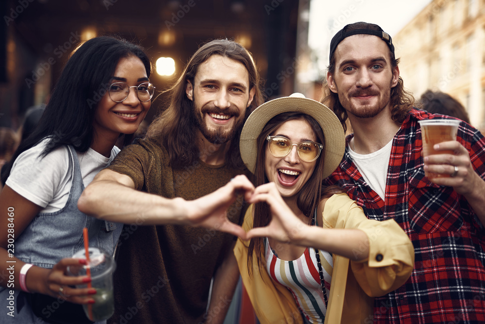 Waist up portrait of young people having fun at outdoor concert. They enjoying drinks and making heart sign Waist up portrait of young people having fun at outdoor concert. They enjoying drinks and making heart sign