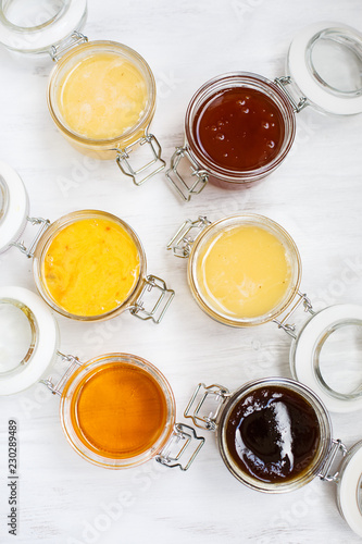 Jars with different kinds of honey in a row on a white wooden background