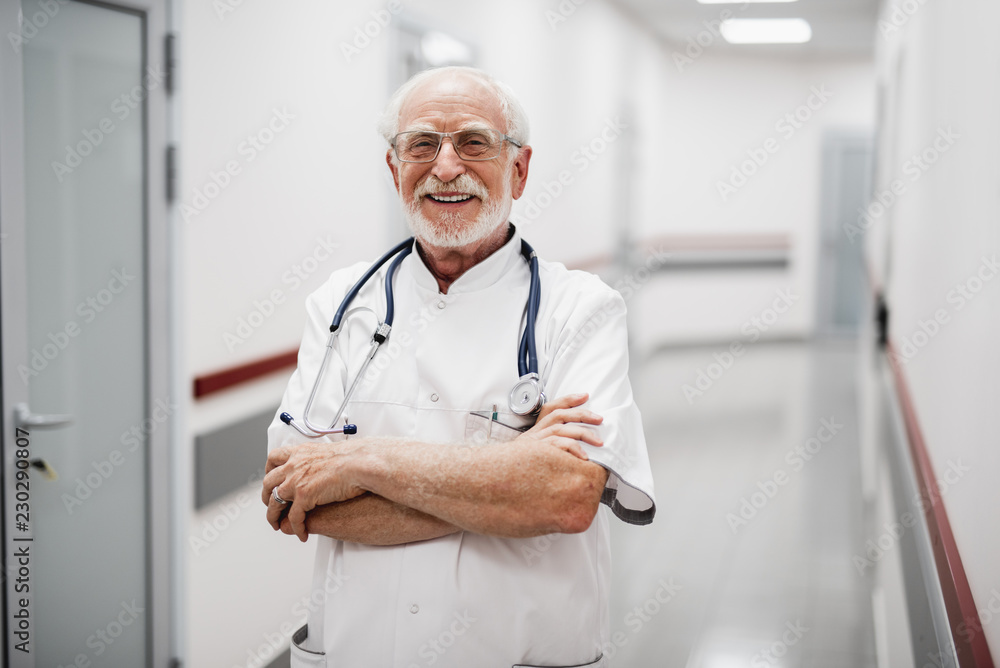 Waist up portrait of bearded gentleman in white lab coat crossing arms and looking at camera with smile Waist up portrait of bearded gentleman in white lab coat crossing arms and looking at camera with smile