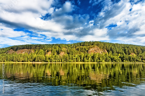 Scenic view on sloped green forestry bank of russia east siberia Yenisei river near krasnoyarsk city with scenery blue sky clouds reflection on still water wonderland panoramic nature background