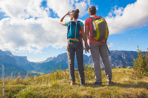 Hikers with backpacks sitting on top of a hill and enjoying mountains view. Dolomiti, Alta Badia