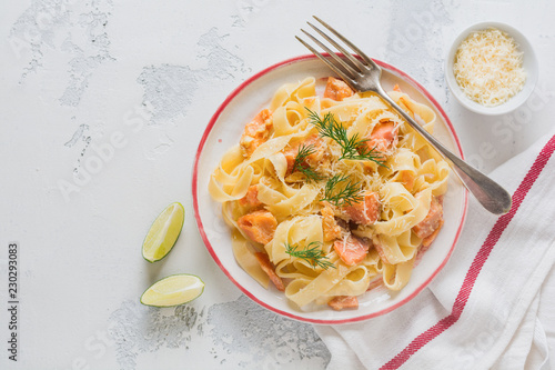 Fettucine pasta with salmon and parmesan cheese in creamy sauce in ceramic plate on old light concrete background. Top view.