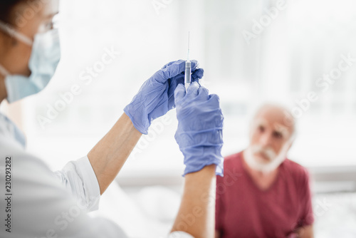 Close up of female medic preparing to make injection. Old man on blurred background