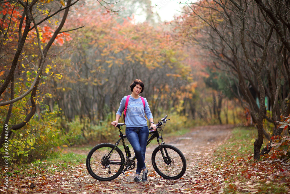 Fototapeta premium The girl on a bike from the rental in the forest. Beautiful young woman posing for the camera in the autumn forest. 