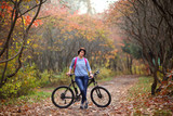 The girl on a bike from the rental in the forest. Beautiful young woman posing for the camera in the autumn forest. 