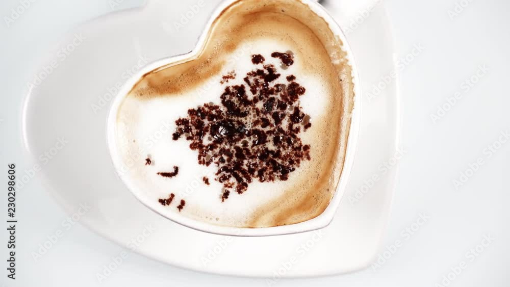 Heart shaped hot coffee cup with milk foam and chocolate decoration rotating on white background. Top down view Heart shaped hot coffee cup with milk foam and chocolate decoration rotating on white background. Top down view