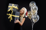 Portrait of beautiful smiling woman in black dress and Santa hat holding stack of gift boxes on the black background. Holding golden balloons and Celebrated a Christmas holiday. Sale concept
