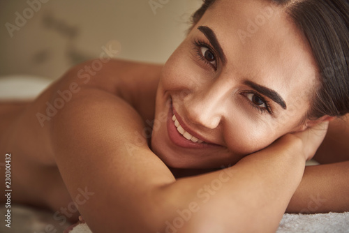 Pretty young lady smiling cheerfully and looking at you while lying on the towel in Turkish bath