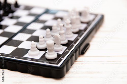 small pocket chess, plastic chess pieces placed on a chessboard on a white wooden background