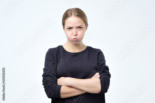 Portrait of beautiful girl frowning her face in displeasure, wearing black sweater, keeping arms folded. Attractive young woman is offended with her boyfriend behavior