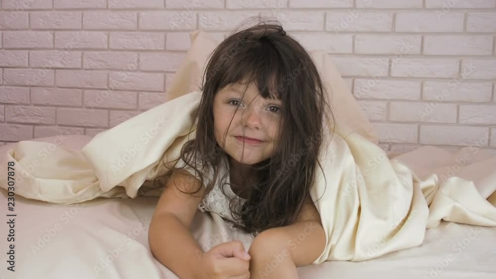 Cheerful child under the covers. The little girl is hiding under a blanket. Cheerful child under the covers. The little girl is hiding under a blanket.