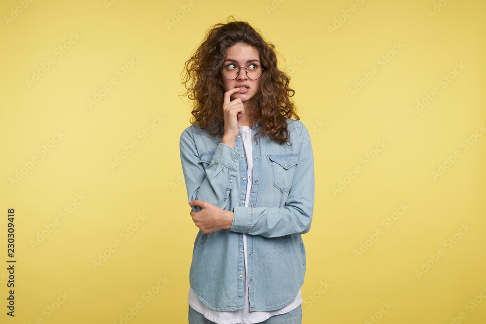 Pretty young woman in eyeglasses thinking of something and looks a side, isolated over yellow background Pretty young woman in eyeglasses thinking of something and looks a side, isolated over yellow background
