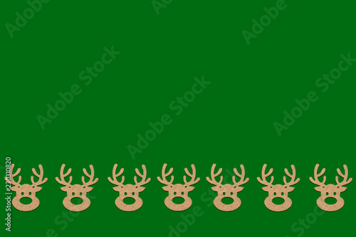 Wooden Christmas toys head of a deer is lined with a pattern on bottom side on a green background. Add text Merry Christmas and Happy New Year. Minimalistic style. Flat lay, top view