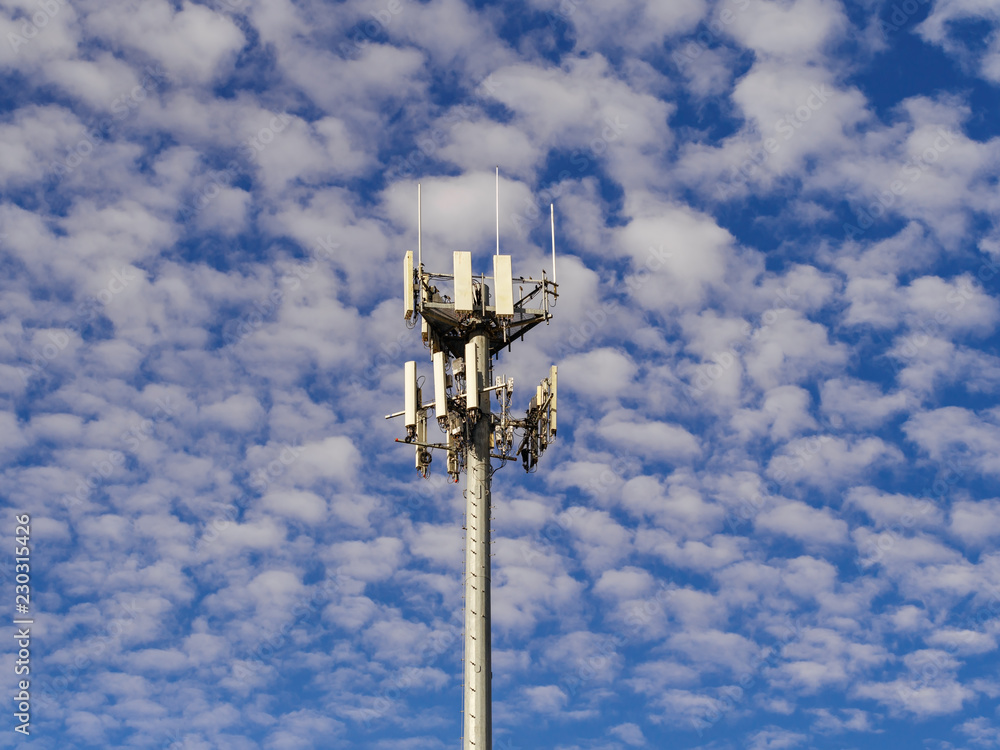 Communications antenna tower against a partly cloudy blue sky.