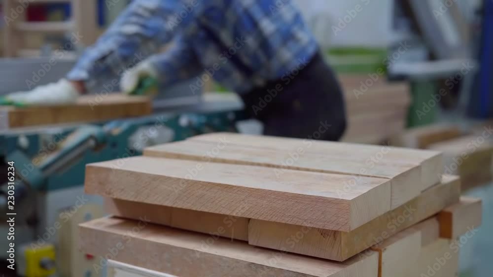 wooden bars are lying in stack, joiner is processing beam in background, then putting it in stack wooden bars are lying in stack, joiner is processing beam in background, then putting it in stack