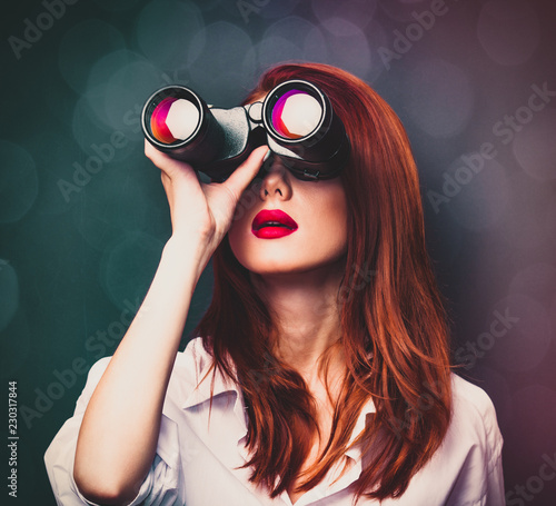 Portrait of a surprised businesswomen in white shirt with binocular on grey background.