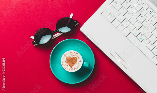 a blue cup, black glasses and laptop lying on the table