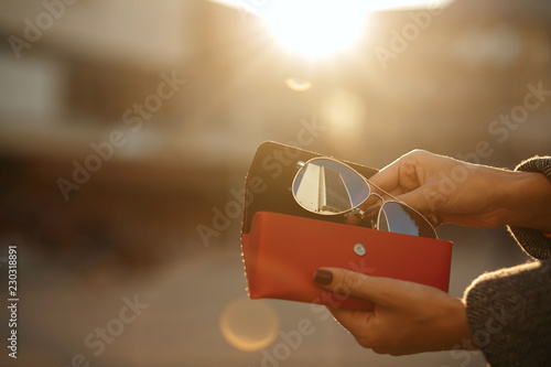 Closeup shot of female hand opening red glasses case at the background of sun. Empty space