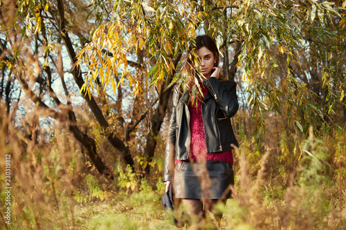 Young woman in park at fall, hiding half of her face under foliage, shallow depth of field