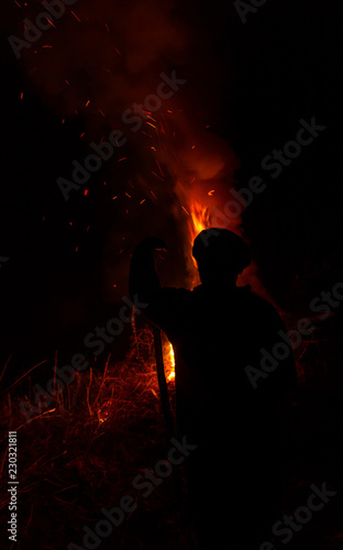 Man with stick silhouette burning dry grass at night