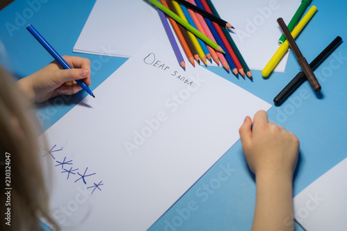 Little girl with pencils and felt-tip pens is writing a letter to Santa