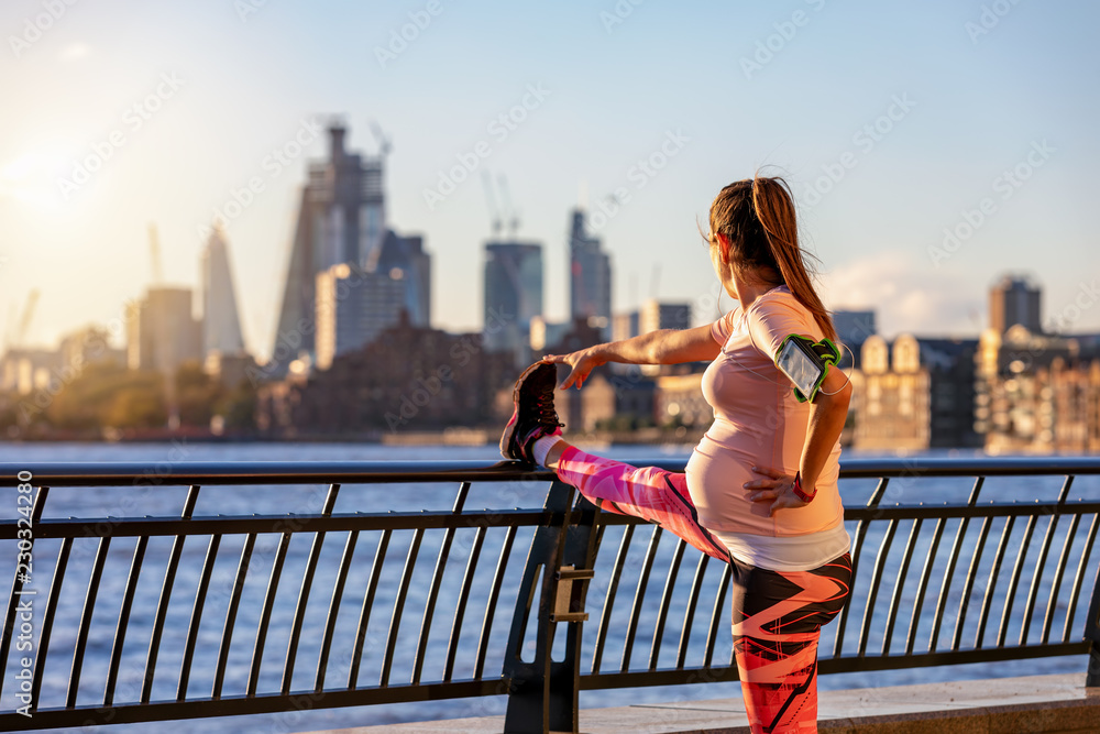 Sportliche, schwangere Frau macht ihre Stretching Übungen vor der Skyline einer Großstadt Sportliche, schwangere Frau macht ihre Stretching Übungen vor der Skyline einer Großstadt