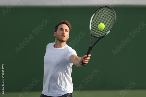 Tennis player man hitting ball playing tennis match on outdoor hard court in fitness club. Male sport athlete healthy lifestyle.