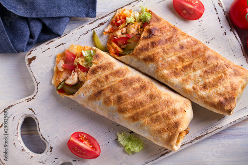 Chicken wraps with tomatoes, pickles, cabbage and onion on white chopping board and wooden table. Tortilla, burritos, sandwiches, twisted rolls