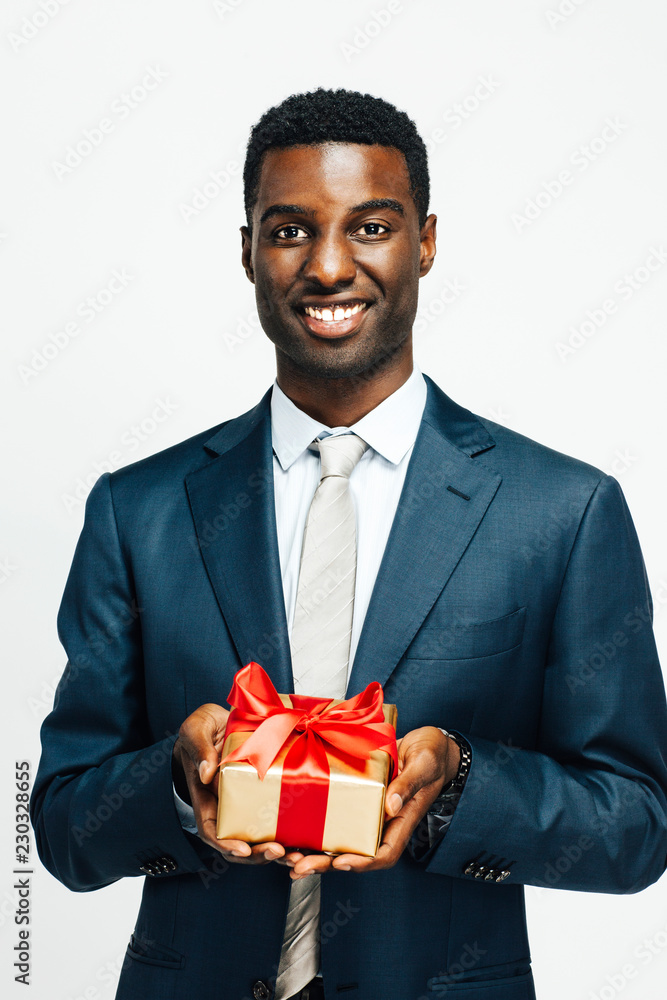 Vertical portrait of a smiling man holding a golden gift tied with a red ribbon, isolated on white studio background Vertical portrait of a smiling man holding a golden gift tied with a red ribbon, isolated on white studio background