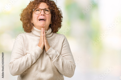 Beautiful middle ager senior woman wearing turtleneck sweater and glasses over isolated background begging and praying with hands together with hope expression on face very emotional and worried