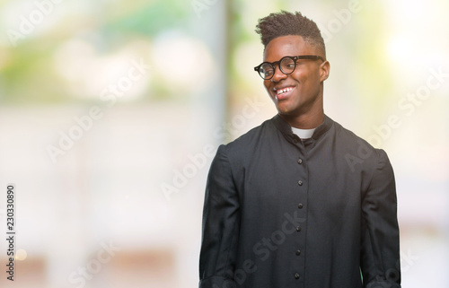 Young african american priest man over isolated background looking away to side with smile on face, natural expression. Laughing confident.
