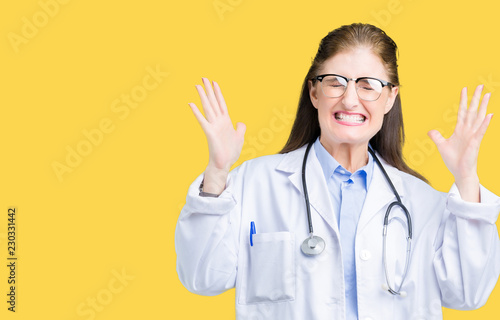 Middle age mature doctor woman wearing medical coat over isolated background celebrating mad and crazy for success with arms raised and closed eyes screaming excited. Winner concept