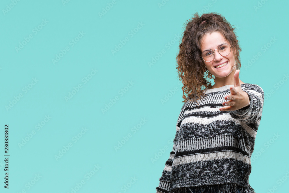 Beautiful brunette curly hair young girl wearing glasses over isolated background smiling friendly offering handshake as greeting and welcoming. Successful business. Beautiful brunette curly hair young girl wearing glasses over isolated background smiling friendly offering handshake as greeting and welcoming. Successful business.