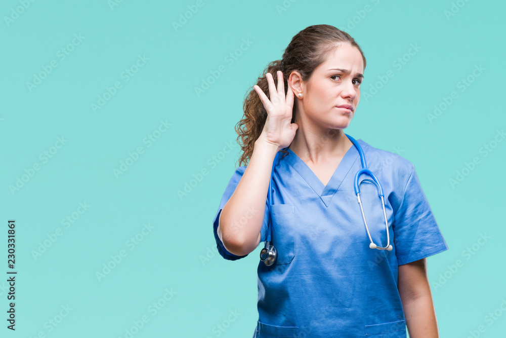 Young brunette doctor girl wearing nurse or surgeon uniform over isolated background smiling with hand over ear listening an hearing to rumor or gossip. Deafness concept. Young brunette doctor girl wearing nurse or surgeon uniform over isolated background smiling with hand over ear listening an hearing to rumor or gossip. Deafness concept.