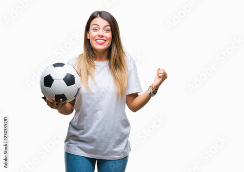 Young beautiful woman holding soccer ball over isolated background screaming proud and celebrating victory and success very excited, cheering emotion