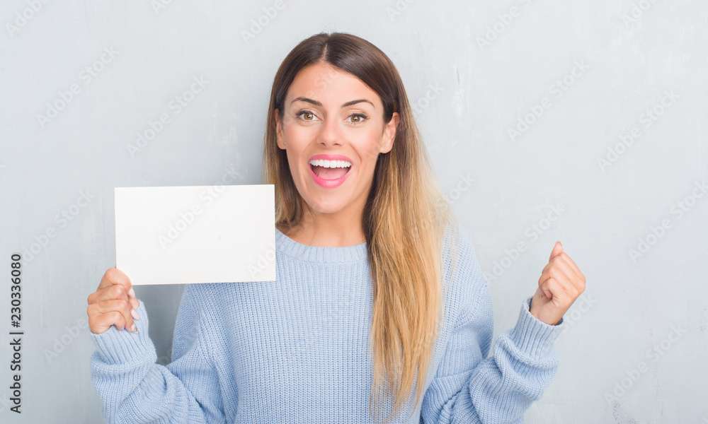 Young adult woman over grey grunge wall holding blank card screaming proud and celebrating victory and success very excited, cheering emotion Young adult woman over grey grunge wall holding blank card screaming proud and celebrating victory and success very excited, cheering emotion