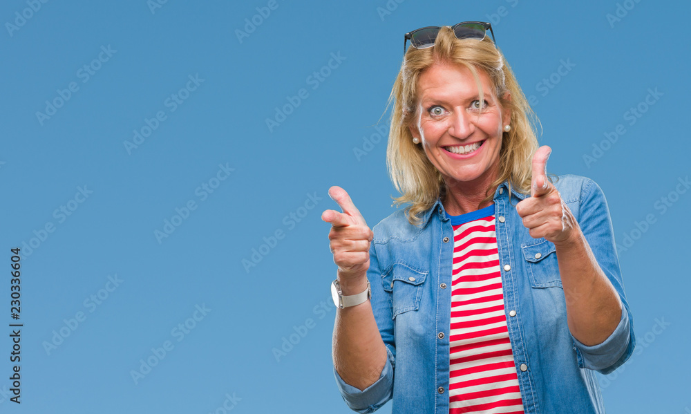 Middle age blonde woman over isolated background pointing fingers to camera with happy and funny face. Good energy and vibes. Middle age blonde woman over isolated background pointing fingers to camera with happy and funny face. Good energy and vibes.