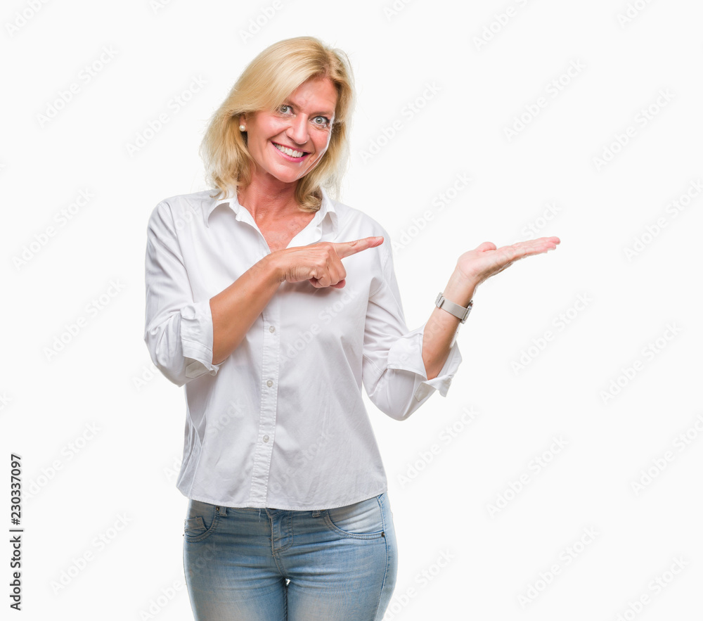 Middle age blonde business woman over isolated background amazed and smiling to the camera while presenting with hand and pointing with finger. Middle age blonde business woman over isolated background amazed and smiling to the camera while presenting with hand and pointing with finger.