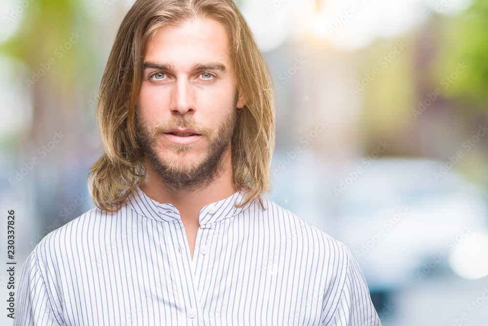 Young handsome man with long hair over isolated background with serious expression on face. Simple and natural looking at the camera. Young handsome man with long hair over isolated background with serious expression on face. Simple and natural looking at the camera.