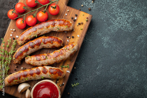 Fried sausages with sauces and herbs on a wooden serving Board. Great beer snack on a dark background. Top view with copy space photo