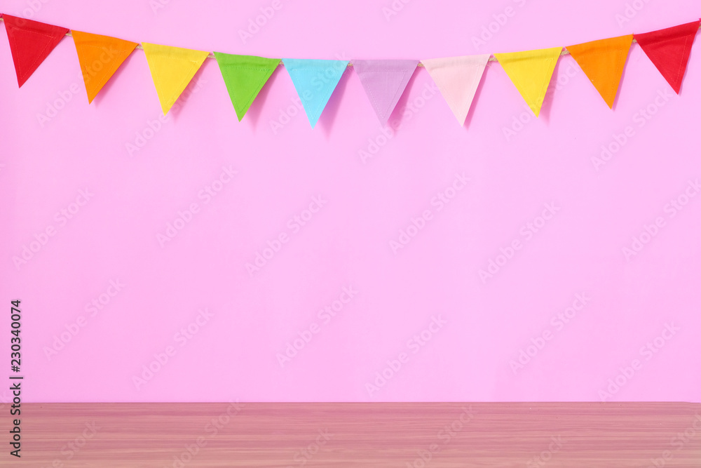 Colorful party flags hanging on pink background and wooden table, birthday, anniversary, celebrate event, festival greeting card background