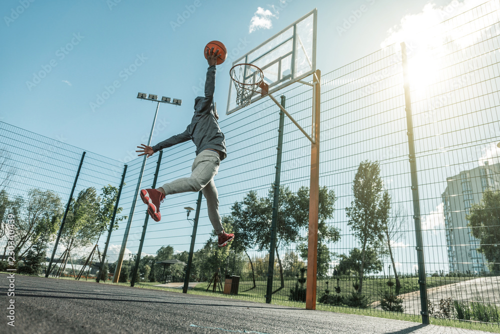 Obraz premium Into the basket. Low angle of a nice young man jumping up while throwing the ball in the basket