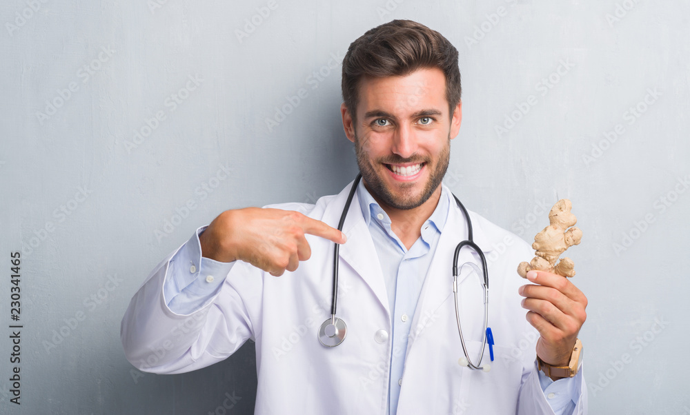 Handsome young doctor man over grey grunge wall holding ginger with surprise face pointing finger to himself Handsome young doctor man over grey grunge wall holding ginger with surprise face pointing finger to himself