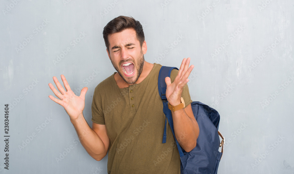 Handsome tourist young man over grey grunge wall wearing backpack celebrating mad and crazy for success with arms raised and closed eyes screaming excited. Winner concept Handsome tourist young man over grey grunge wall wearing backpack celebrating mad and crazy for success with arms raised and closed eyes screaming excited. Winner concept
