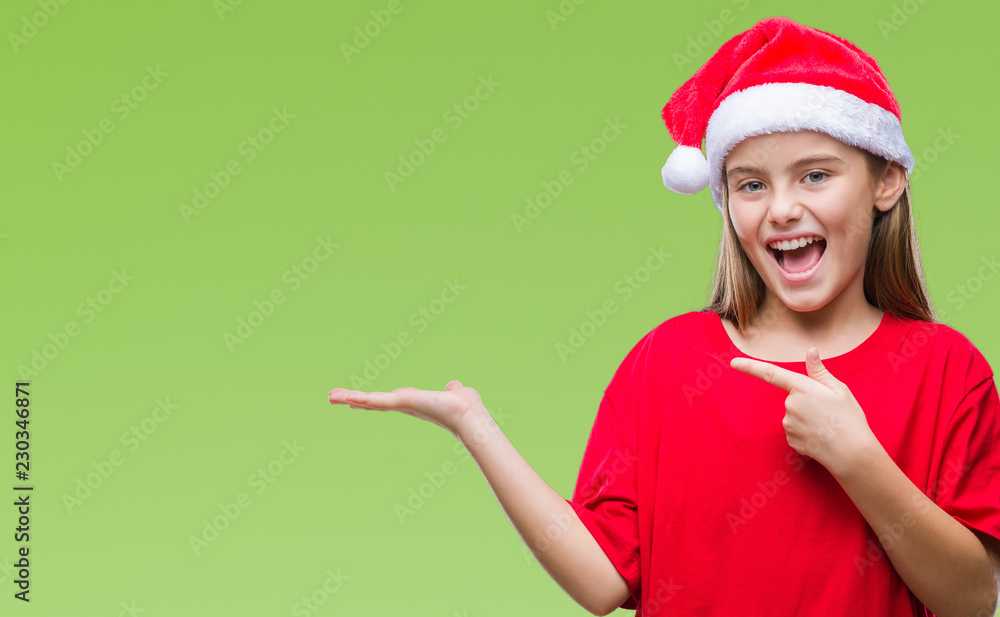 Young beautiful girl wearing christmas hat over isolated background amazed and smiling to the camera while presenting with hand and pointing with finger. Young beautiful girl wearing christmas hat over isolated background amazed and smiling to the camera while presenting with hand and pointing with finger.