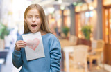 Young beautiful girl giving mother father day card with red heart over isolated background scared in shock with a surprise face, afraid and excited with fear expression