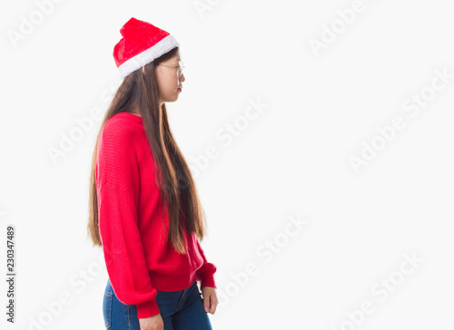 Young Chinese woman over isolated background wearing christmas hat looking to side, relax profile pose with natural face with confident smile.