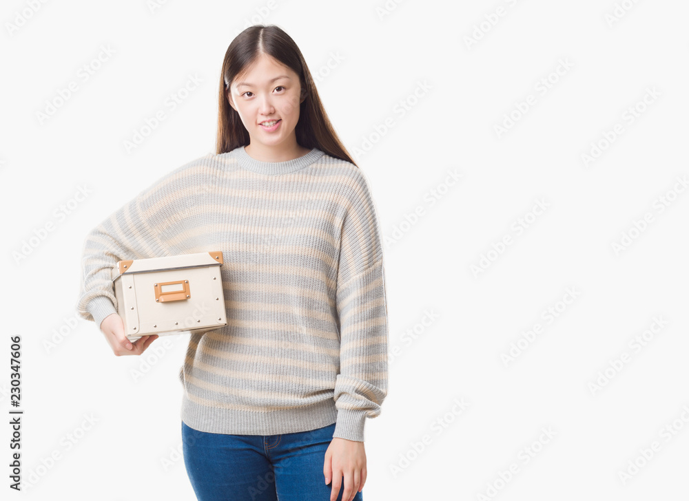 Young Chinese woman over isolated background holding a box with a happy face standing and smiling with a confident smile showing teeth Young Chinese woman over isolated background holding a box with a happy face standing and smiling with a confident smile showing teeth